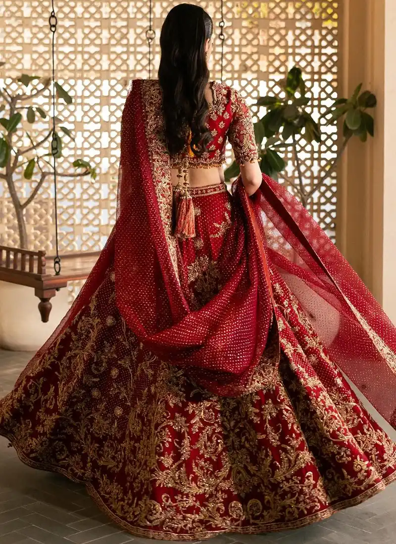 Deep red lehenga choli in three-quarter front view with ornate gold blouse embroidery and flowing sheer dupatta