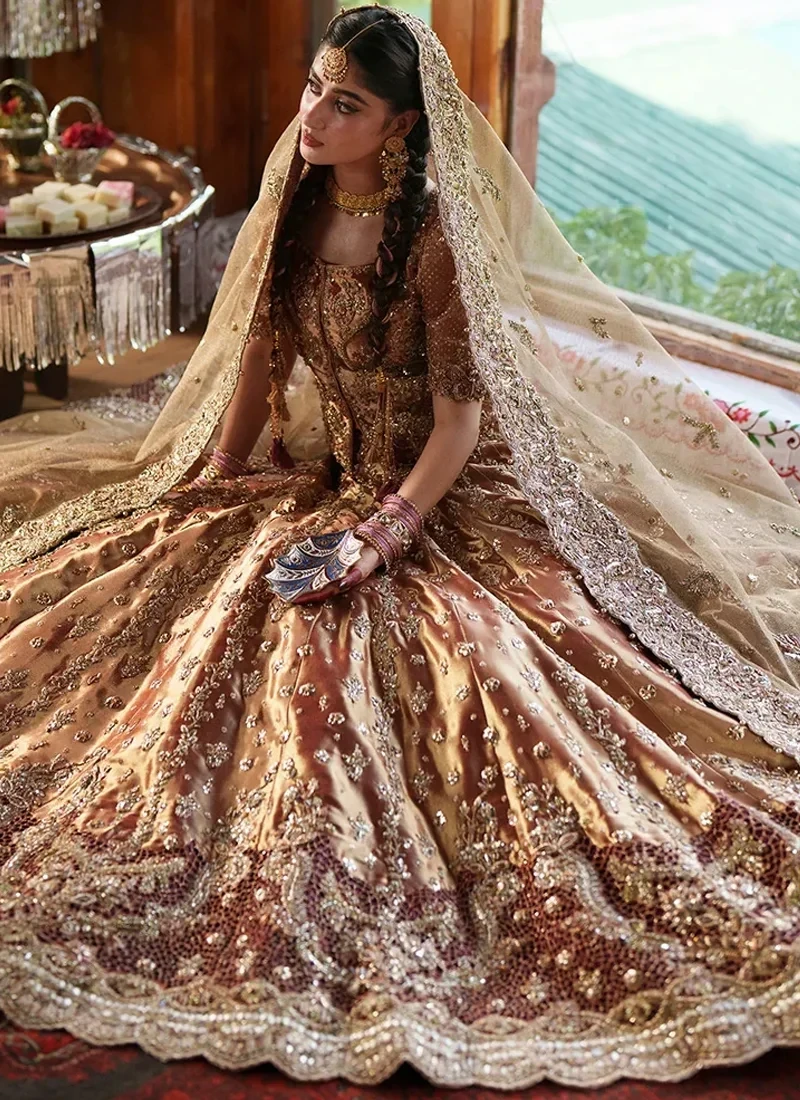 Seated view of the copper-gold lehenga spread in a wide circle, showing the scalloped hem over a dark lattice-like border and the champagne dupatta