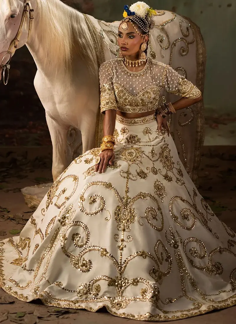 Ivory lehenga choli bodice close-up with pearl-dotted sheer yoke, gold floral embroidery and ornate sleeve cuffs