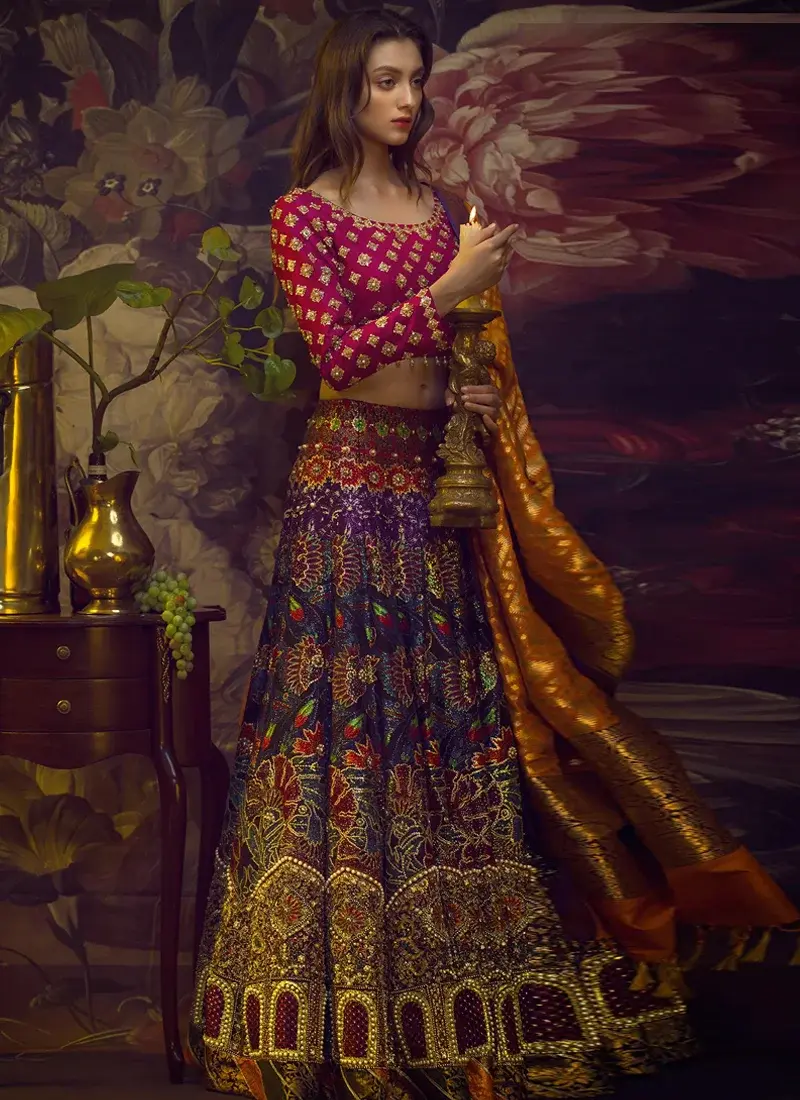 Multicolor mehndi lehenga seated side view showing bold embroidered flowers and a detailed gold arch border