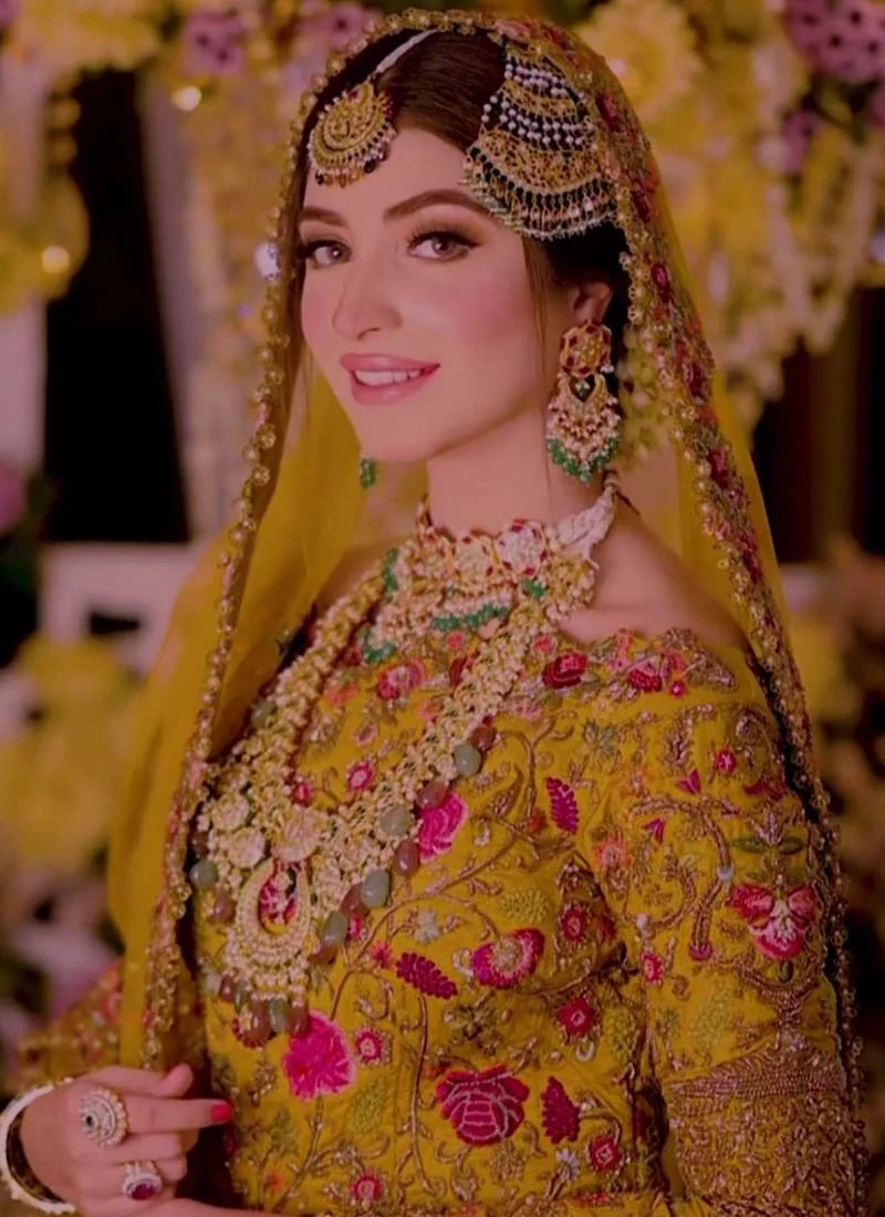 Mustard gold bridal lehenga bodice close-up with off-shoulder neckline and intricate pink floral embroidery