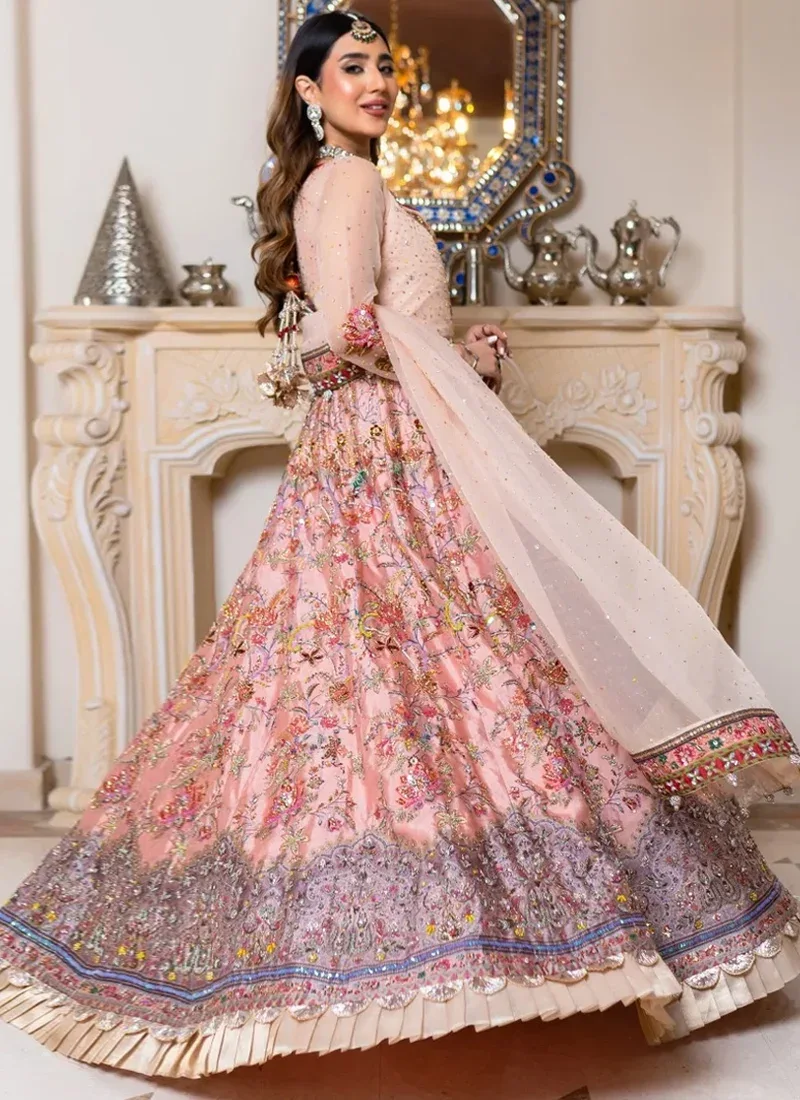 Salmon pink Nikkah Anarkali maxi in a seated front view with multicolour floral embroidery across the flared skirt